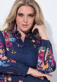 Marineblaues Blumenbluse mit lebhaften rosa, blauen und gelben Blumen; verfügt über einen Kragen, Knopfleiste und Ausschnittdetails an den Ärmeln.