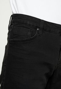 Black denim jeans with a slim fit, featuring a front pocket and a button closure. The fabric has a smooth texture and minimal fading.