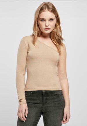 Beige långärmad topp med asymmetrisk halsringning, figurnära design, slät textur och subtila sömmar, kombinerad med mörkgrå jeans.