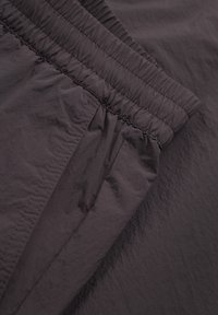 Vêtement violet foncé doté d'une taille élastique froncée et d'un tissu lisse et léger. Surface texturée avec un léger éclat et des coutures soignées.