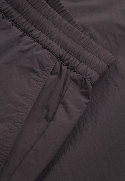 Vêtement violet foncé doté d'une taille élastique froncée et d'un tissu lisse et léger. Surface texturée avec un léger éclat et des coutures soignées.