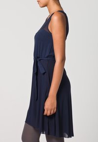 Robe sans manches bleu marine avec un corsage ajusté et une jupe évasée, dotée d'une ceinture à nouer à la taille et d'un tissu doux et texturé.