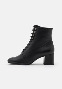 Botas de tobillo de cuero negro con punta afilada, presentan cordones frontales y ojales metálicos, sustentadas por un tacón grueso.