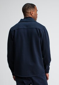 Marineblauwe fleece shirt met een kraag, lange mouwen en een ontspannen pasvorm. Beschikt over stikdetails en een afgeronde zoom voor comfort.