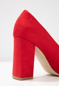 Roter hoher Schuh aus weichem, strukturiertem Material. Verfügt über einen dicken Absatz und ein spitzes Design mit einem glatten Innenfutter.