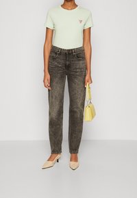 Světle zelené tričko s krátkým rukávem a malým trojúhelníkovým logem, spárované s faded černými džíny s vysokým pasem a béžovými jehlovými lodičkami. Žlutá kabelka.