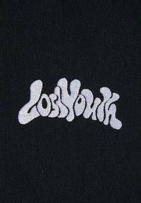 Sort stof med en struktureret overflade prydet med hvid, bølget broderet tekst, der lyder "LOSS YOUTH." Teksten har en legesyg skrifttype.