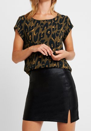 Haut à manches courtes avec un imprimé léopard vert et noir, associé à une mini-jupe en cuir synthétique noire avec une fente sur le côté.