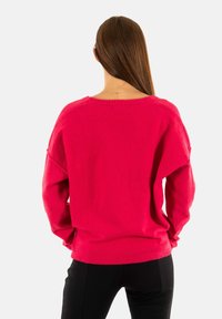 Helderroze trui gemaakt van een zachte, gestructureerde stof. Heeft een ontspannen pasvorm, lange mouwen en een geribde zoom. De achterkant toont verlaagde schouders.