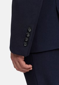 Navy blazer z detalami z teksturowanej tkaniny, z czterema czarnymi guzikami z kwiatowym wzorem na mankietach oraz elegancką, dopasowaną sylwetką.