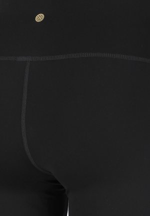 Leggings noirs en tissu extensible, dotés d'un design sans couture, de coutures à plat et d'un petit logo doré près de la taille.