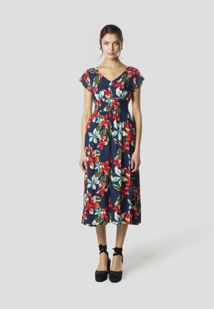 Vestido floral navy con mangas cortas y cintura fruncida, con grandes flores rojas y blancas, combinado con zapatos de plataforma negros.