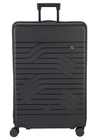 Valigia rigida nera con una superficie testurizzata a onde, manico retrattile e quattro ruote per la mobilità. Presenta un logo circolare sul davanti.