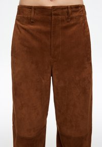 Bruine suède broek met een gladde textuur, voorzien van een rechte snit, riemlussen en gestikte details langs de naden en zakken.