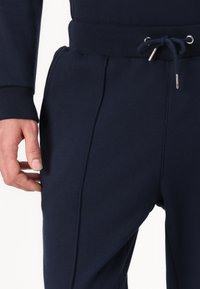 Marineblauwe joggingbroek met een geribde tailleband, trekkoordsluiting en zijzakken; gemaakt van zachte, gemêleerde stof met vlakke naden.