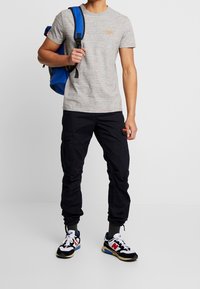 Šedé marl tričko s krátkým rukávem, spárované s černými cargo kalhotami s kapsami. Černé a modré tenisky dotvářejí celý outfit. Součástí je modrý batoh.