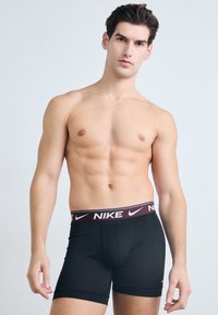 Crne Nike bokserice s maroon pojasom na kojem se nalazi Nike logo. Glatka tkanina s uskim dizajnom i detaljem na prednjem dijelu.
