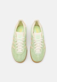 Πράσινα σουέτ αθλητικά παπούτσια με μπεζ λεπτομέρειες και λευκές κορδέλες. Διαθέτουν σχέδιο με τρεις ρίγες, μαλακή σόλα και σόλα από καουτσούκ.