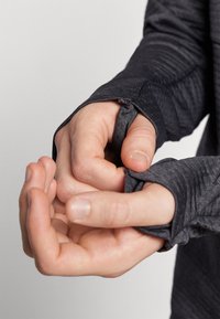Langermet skjorte i mørkegrått stoff, med tommelhull i mansjettene, strukturert mønster og tettsittende design rundt håndleddene.