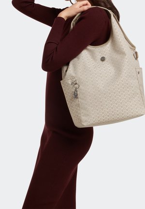 Sac fourre-tout beige à motifs avec une quincaillerie argentée et un charm décoratif, offrant un grand compartiment principal et des poches latérales.