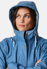 Wodoodporna niebieska kurtka przeciwdeszczowa z kapturem, z zapięciem na zamek, zatrzaskami, akcentami w postaci sznurków oraz miękką podszewką.