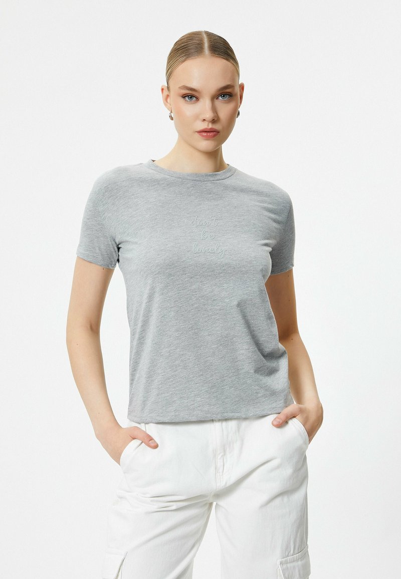 Heather grå T-shirt med korte ærmer, rund halsudskæring og lysegrøn broderet tekst "vær ikke alene" på forsiden.