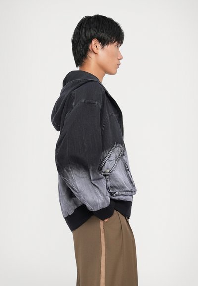 Denim jacket with a hood, featuring a gradient from black to gray, ribbed cuffs, and a side pocket. Smooth texture with subtle stitching details.