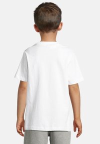 B altā kokvilnas T-kreklā ar īsām piedurknēm, apaļo kakla izgriezumu un brīvu piegriezumu, skatoties no aizmugures. Ikdienas stils, bez rakstiem vai akcentiem.