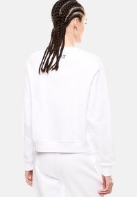 Sudadera blanca cortada con un dobladillo acanalado, cuello redondo y logotipo bordado en la parte posterior. Textura suave, fit relajado.