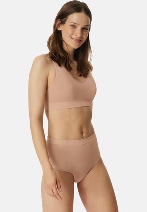 Donna con capelli castani che indossa un reggiseno senza cuciture color nudo abbinato a mutandine a vita alta, sorridente, su uno sfondo chiaro e uniforme.