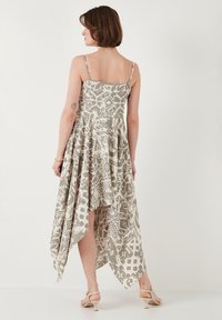 Hoog-laag jurk in lichtbeige met een gestructureerd abstract patroon. Spaghetti bandjes en een vloeiende silhoette, met een asymmetrische zoom.