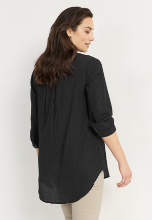Zwarte, gestructureerde shirt met een iets losse pasvorm, lange mouwen opgestroopt en een gebogen zoom. Heeft een knoopsluiting bij de manchetten.