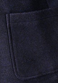 Jūras spēku vilnas audumam ir teksturēta virsma ar redzamu kabatu un smalkām šuvēm gar malām.