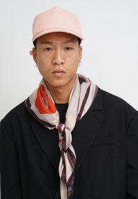 Pink cap with a structured design, paired with a patterned silk scarf featuring shades of red, beige, and brown, worn over a black jacket.