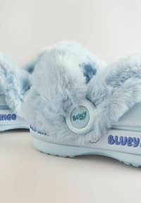Ciabatte azzurro chiaro con morbido peluche sintetico, caratterizzate da una forma arrotondata, dettaglio con bottone e logo "Bluey", e suole in gomma testurizzata.