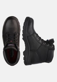 Schwarze Arbeitsstiefel haben ein oberes Material aus strukturiertem Leder und eine Gummisohle, mit Metallösen und einem gepolsterten Schaft für zusätzlichen Komfort.