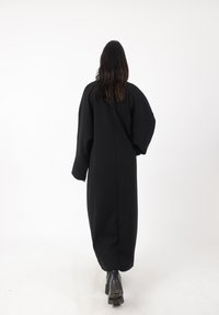Schwarzes, langärmliges Kleid mit lockerer Passform, aus einem dickeren Stoff gefertigt. Der Rücken ist gerade, und das Kleid hat ein einfaches, minimalistisches Design.
