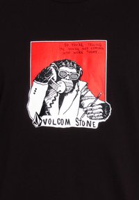 Schwarzes Shirt mit einem Motiv eines Affen im Anzug, der ein Telefon hält, mit Text darüber. Unten mit "VOLCOM STONE" brandmarkiert.