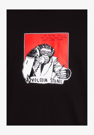 Camiseta negra con un gráfico de un mono en traje sosteniendo un teléfono, con texto arriba, marcado con "VOLCOM STONE" en la parte inferior.