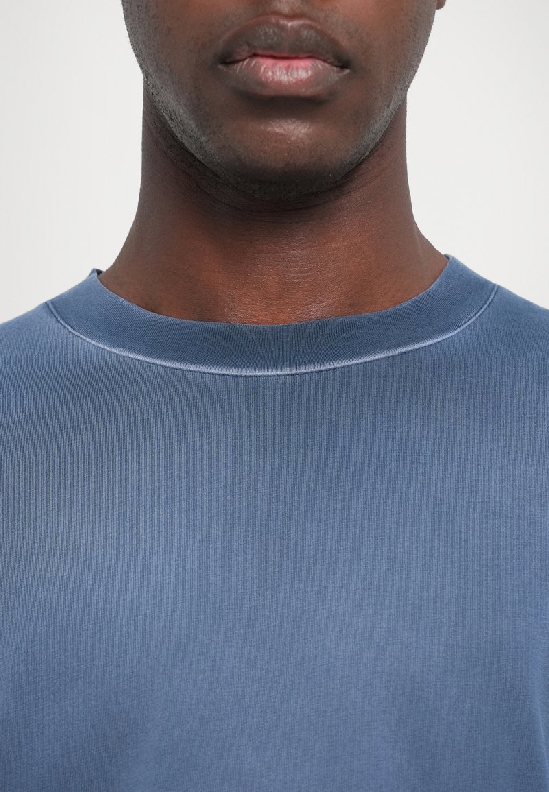 Blaues Rundhals-T-Shirt aus glattem, leichtem Stoff. Verfügt über eine dezente gerippte Textur, ohne sichtbare Muster oder Akzente.