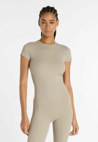 Maglietta beige a maniche corte con colletto rotondo, forma aderente, texture morbida e finitura liscia, abbinata a leggings coordinati.