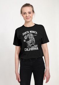 Camiseta negra con texto gráfico en blanco que presenta un tigre y elementos de diseño "Santa Monica". Mangas cortas, cuello redondo.