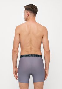 Sivé boxerky s hladkou textúrou, s čiernym pásom s nápisom "ARMOR" v tyrkysovom písme. Zadný pohľad ukazuje priliehavý strih.