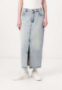 Lyseblå denimskjørt med frontslitt, har klassisk femlommers design, knapp- og glidelås-lukking, og en rett silhuett, paret med hvite sneakers.