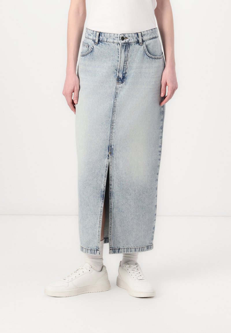 Lyseblå denimskjørt med frontslitt, har klassisk femlommers design, knapp- og glidelås-lukking, og en rett silhuett, paret med hvite sneakers.