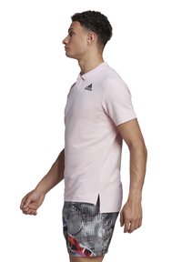 Polo shirt rose clair avec un tissu texturé, manches courtes et col à boutons. Logo Adidas noir sur la poitrine gauche.