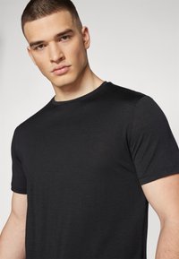 Camiseta negra de cuello redondo, hecha de una tela suave, con mangas cortas y un diseño ajustado. Sin patrones visibles ni detalles metálicos.