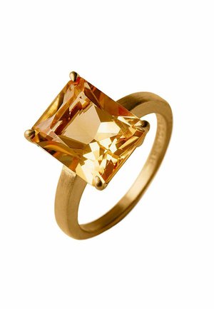 Anillo de oro con una gran gema amarilla de corte cuadrado sostenida por cuatro garras en una banda circular lisa sobre un fondo blanco.