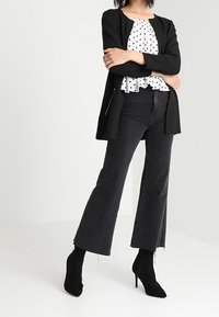 Svart cardigan över en vit topp med pricka och peplum, matchad med höga svarta vida jeans och svarta spetsiga ankelstövlar.