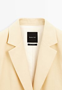 Blazer beige clair avec col à revers cranté et étiquette intérieure indiquant Massimo Dutti, fabriqué au Portugal.